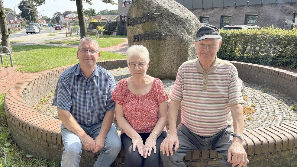 Die Ortsratsmitglieder Ernst-Ingo Lind (von links), Karin Moch und Ortsbürgermeister Karl-Heinz Jesionek sitzen auf der Mauer des Rondells, in dem sich der große Findling mit der Aufschrift Flachsmeer befindet. Foto: Carsten Ammermann