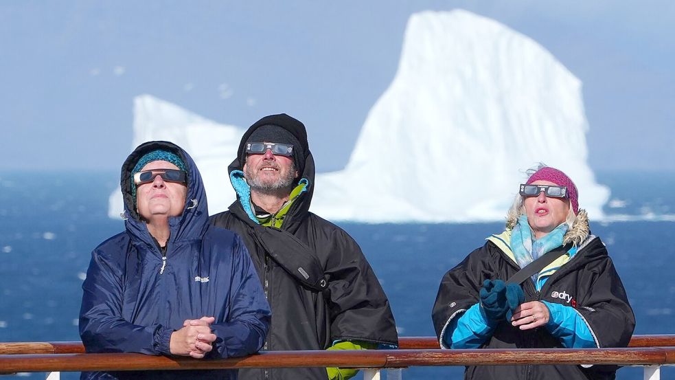 Passagiere an Bord des Kreuzfahrtschiffs „Ambition“ der Reederei Ambassador beobachten mit speziellen Sonnenfinsternisbrillen den Beginn der totalen Sonnenfinsternis vor der Küste Grönlands. Foto: Owen Humphreys
