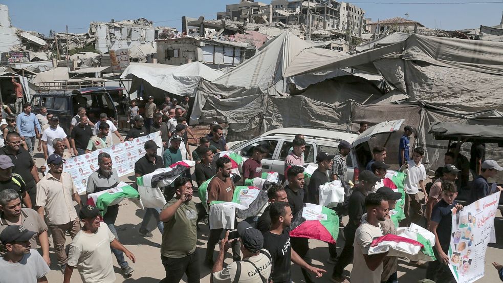 Palästinenser tragen am 20. August 2026 in Gaza-Stadt die Leichen von Angehörigen während einer Massenbeerdigung für 50 Menschen, deren sterbliche Überreste aus den Trümmern von Gebäuden geborgen wurden, die durch israelische Luftangriffe zerstört worden waren. Foto: Mohammad Abu Elsebah/ZUMA Press Wire/dpa