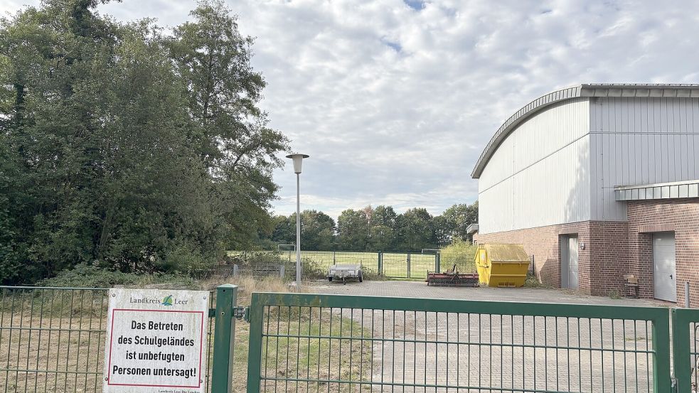 Blick durch das geschlossene Eingangstor auf das Schulgelände an der Werftstraße in Rhauderfehn. Im Hintergrund ist ein Rasenplatz mit Fußballtor zu sehen. Dort plant die Gemeinde eine neue Sportanlage mit Kunstrasenplatz und Leichtathletikanlage. Foto: Horst Kruse