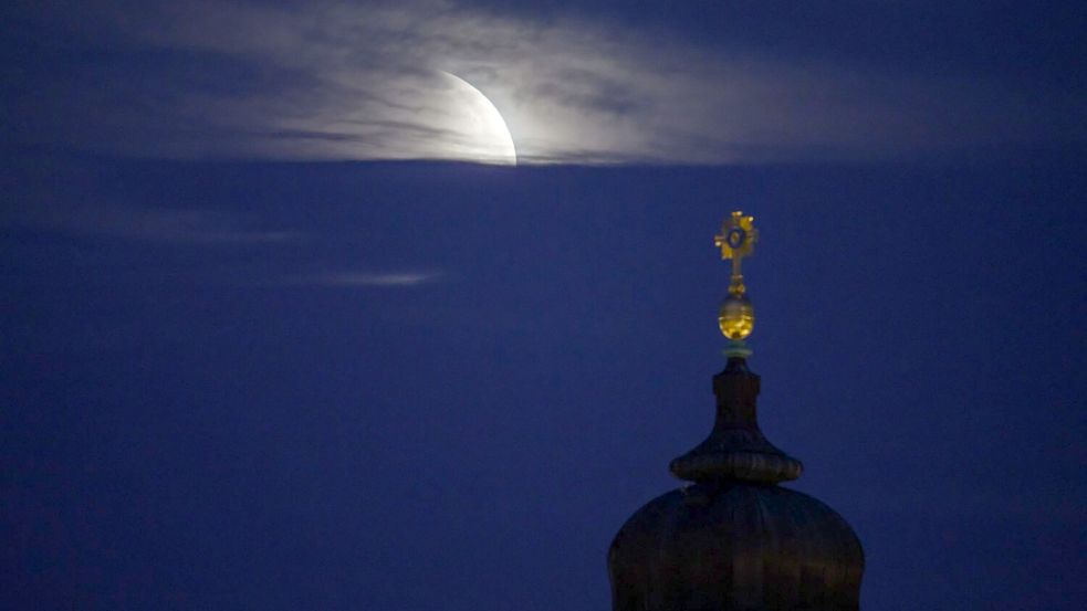 Der Mond geht am Morgen während einer partiellen Mondfinsternis hinter dem Kreuz der Frauenkirche unter. Foto: Robert Michael