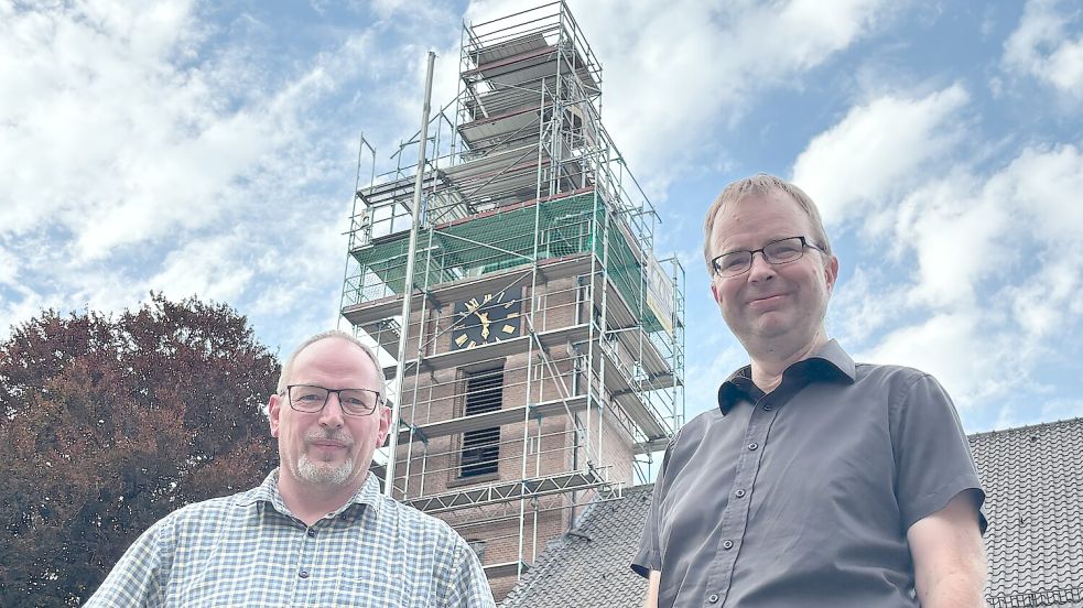 Pastor Holger Rieken (rechts) und Lars Redemske, Vorsitzender des Bauausschusses der Ostrhauderfehner Kirchengemeinde, stehen vor dem eingerüsteten Turm der Petruskirche. Foto: Henrik Zein