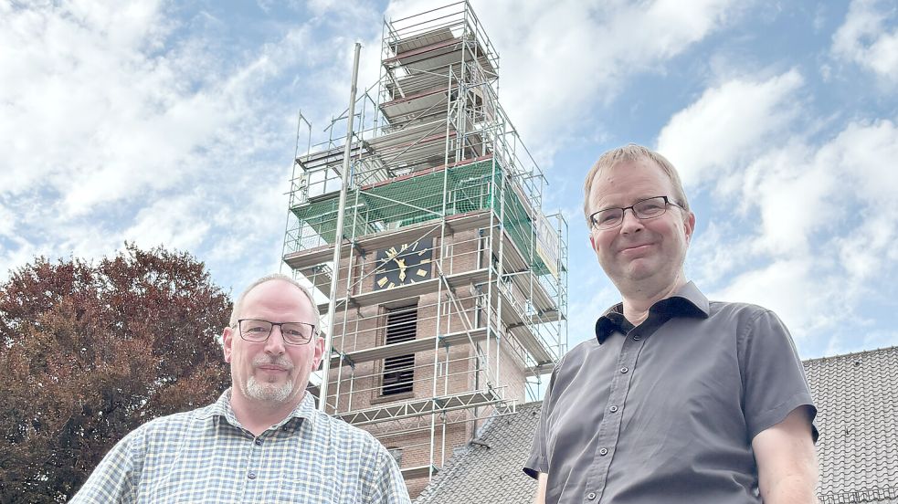 Pastor Holger Rieken (rechts) und Lars Redemske, Vorsitzender des Bauausschusses der Ostrhauderfehner Kirchengemeinde, stehen vor dem eingerüsteten Turm der Petruskirche. Foto: Henrik Zein