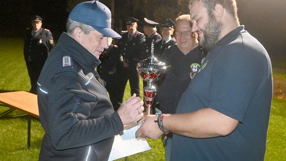 Rhaudermoors Ortsbrandmeister Hauke Bohlen (rechts) übergibt den Siegerpokal an Hilmar Schulte (links), Gruppenführer der siegreichen Wettkampfgruppe aus Holte. Foto: Holger Weers