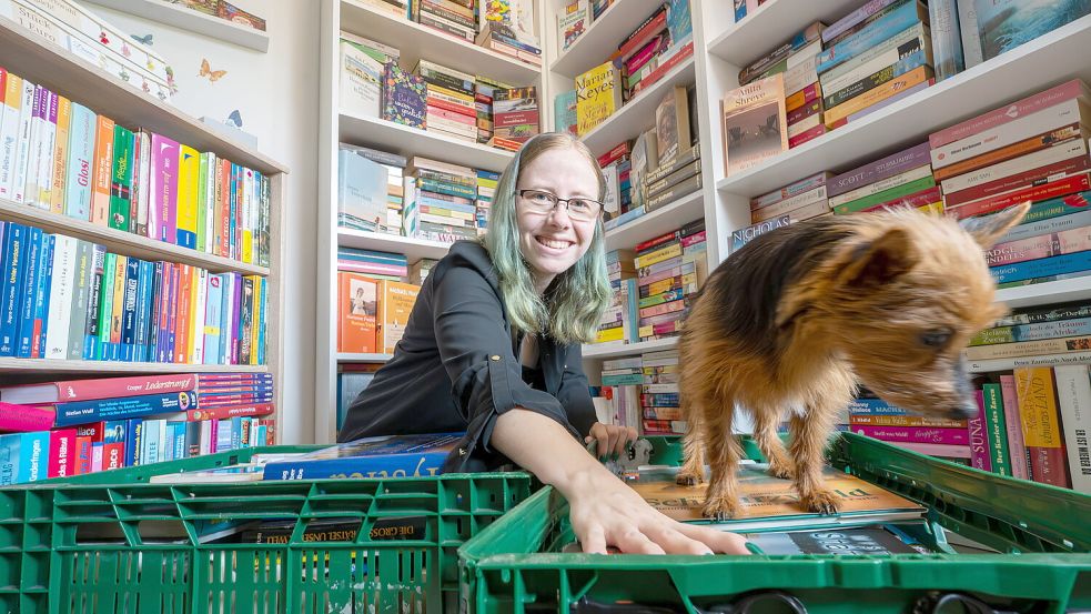 Diana Rösemann hockt mitten in ihrem Bücherraum in Remels. Hündin Luna steht auf einer der Bücherkisten. Foto: Klaus Ortgies