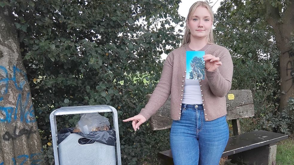 Kim Böckler mit einem Foto ihres Katers Mucki vor dem Mülleimer am Leda-Jümme-Weg, wo das Tier tot aufgefunden wurde. Foto: Clarissa Scherzer
