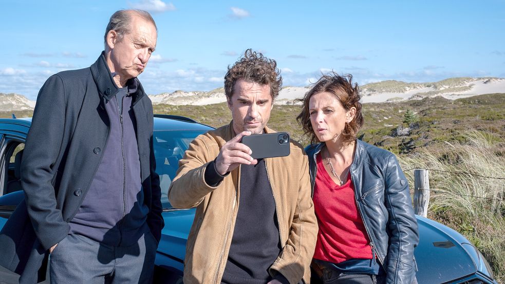 Carl Sievers (Peter Heinrich Brix), Hinnerk Feldmann (Oliver Wnuk) und Ina Behrendsen (Julia Brendler, v. l.) stehen vor dem Auto und schauen sich gemeinsam etwas auf Feldmanns Handy an Foto: ZDF/Manju Sawhney