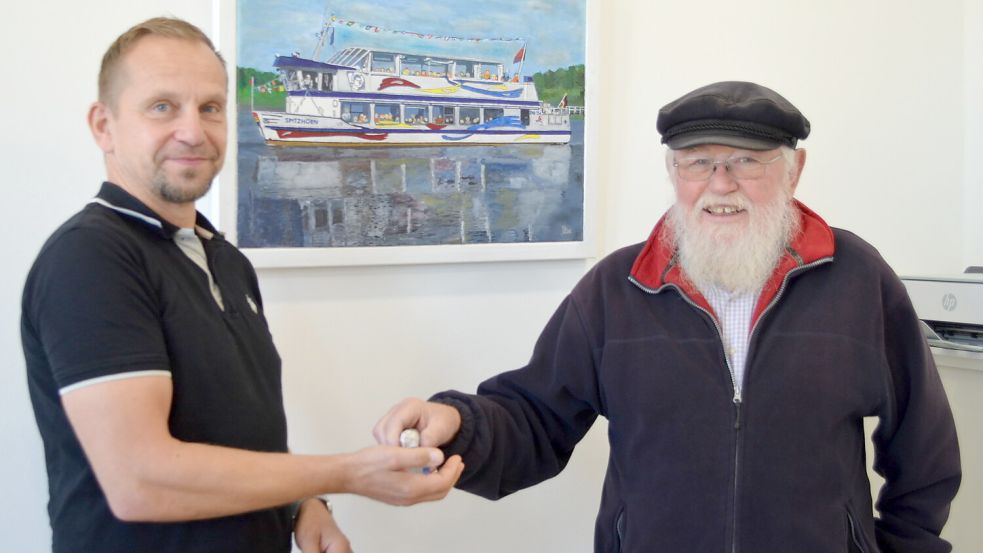Schlüsselübergabe: Nach fast 20 Jahren übergibt Egon Buß (rechts) aus Elisabethfehn die Schlüssel für den Ausflugsdampfer der Touristik Barßel-Saterland, die MS Spitzhörn, an deren Geschäftsführer Jens Lindstädt. Mit 79 Jahren möchte Buß das Steuerruder aus der Hand geben. Hinter den Beiden hängt ein Bild in Lindstädts Büro, das der frühere Barßeler Lehrer Horst Droste von der MS Spitzhörn gemalt hat. Foto: Astrid Fertig